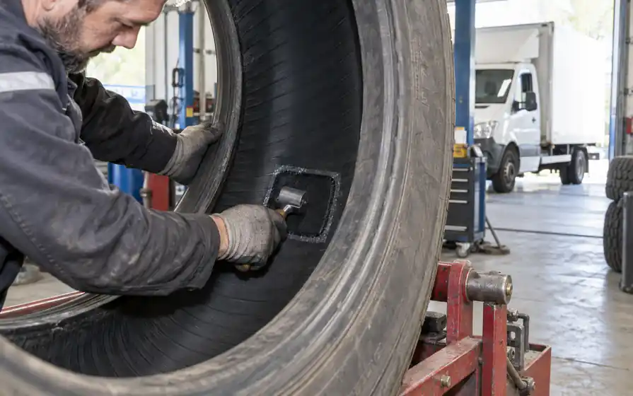 Technician rolling an internal repair patch inside a demounted commercial tyre held open on a spreader.